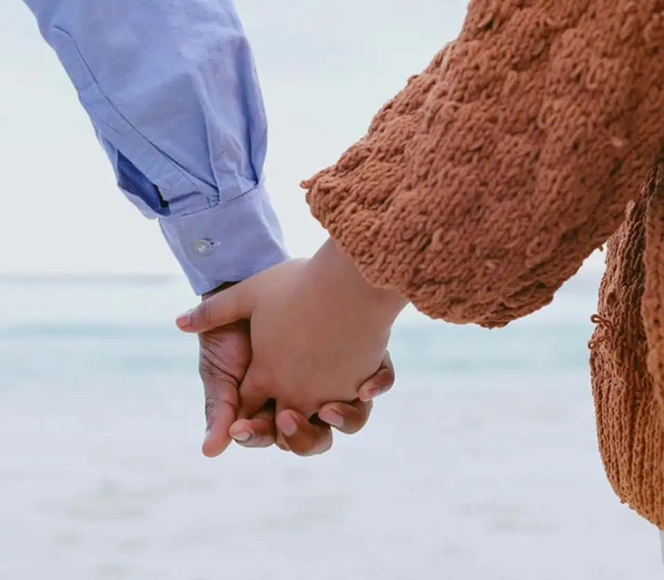 Close-up of two people holding hands on the beach.
