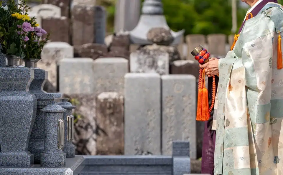 Person in traditional kimono holding a small object at a memorial site.
