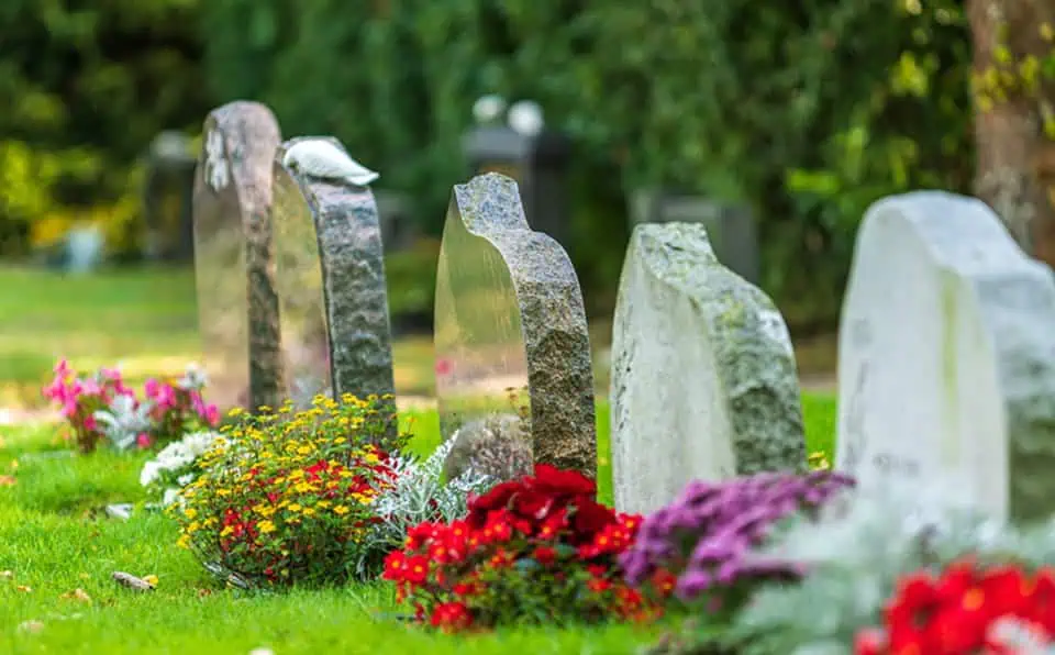 Multiple gravestones with colorful flowers in a cemetery setting.