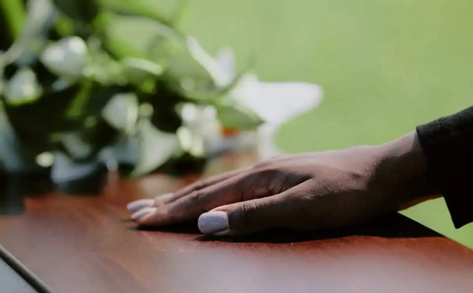 Close-up of a hand resting on a wooden surface during a memorial service.