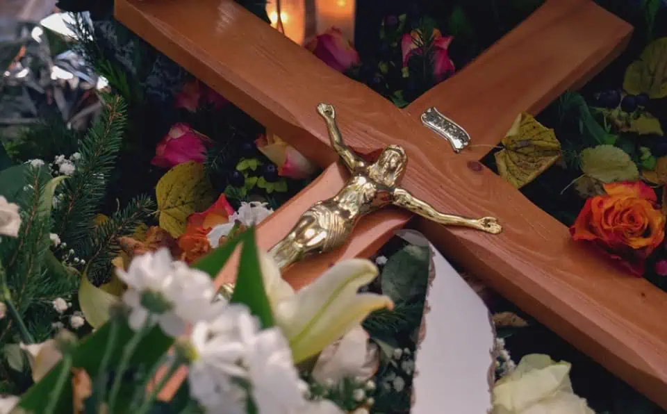 Close-up of a wooden cross with a gold crucifix and floral arrangement.