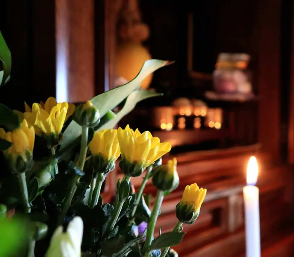 Close-up of yellow flowers and a lit candle at a memorial altar.