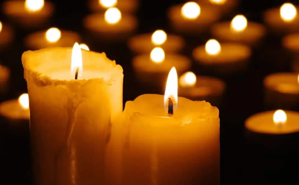 Two lit candles with blurred candles in background, memorial setting.