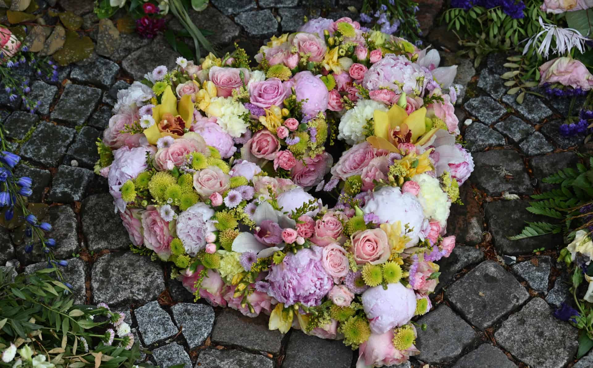 Colorful floral heart arrangement on cobblestone ground.