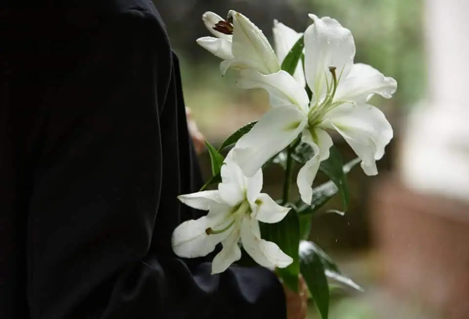 Person holding a bouquet of white lilies in a memorial setting.