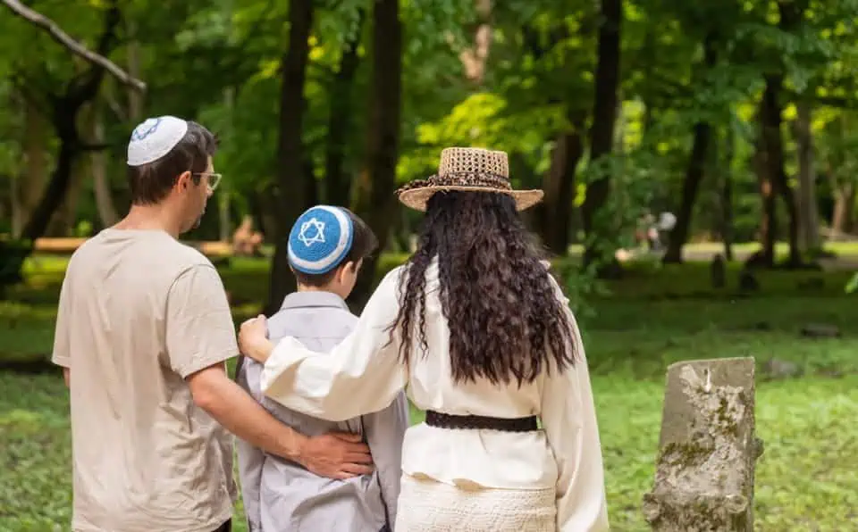 Family with child and woman in park, holding hands, surrounded by trees.