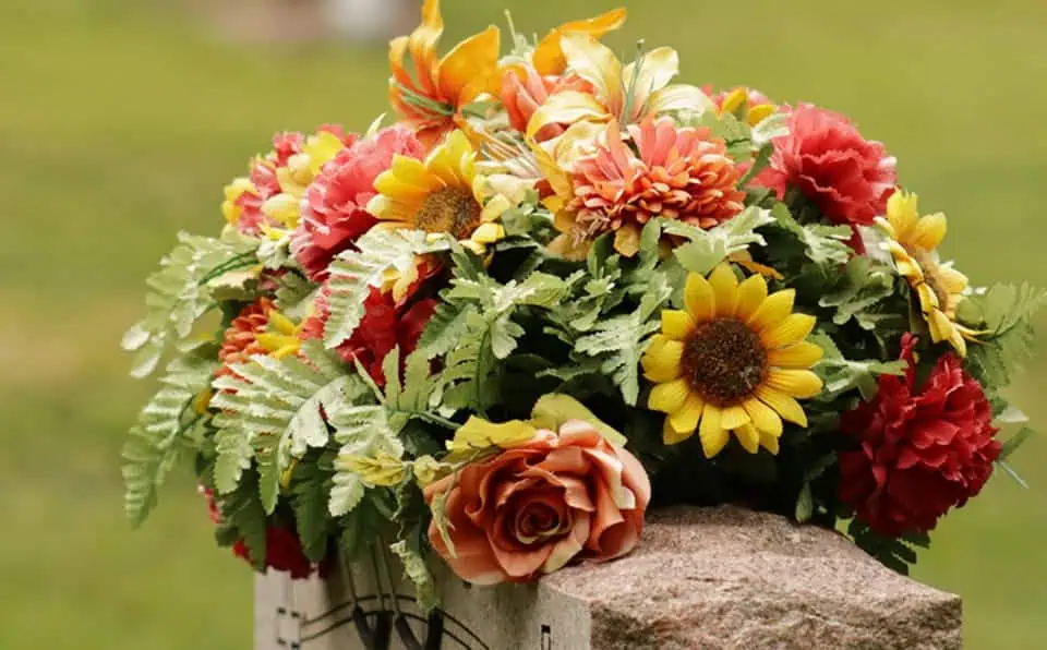 Colorful flower arrangement with sunflowers, roses, and dahlias on a stone.