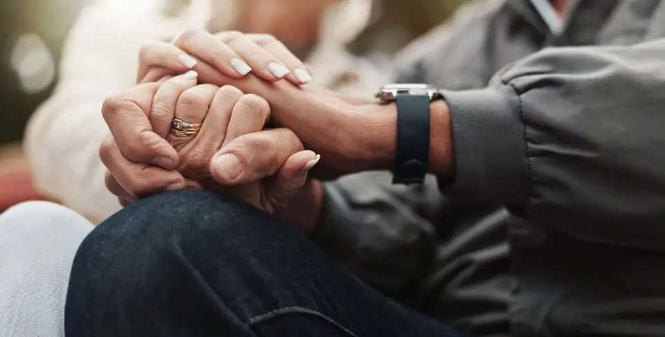 Close-up of two people holding hands, showing support and compassion.