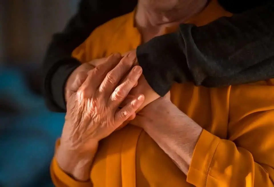 Close-up of two people hugging, one wearing a black sleeve and the other in orange.