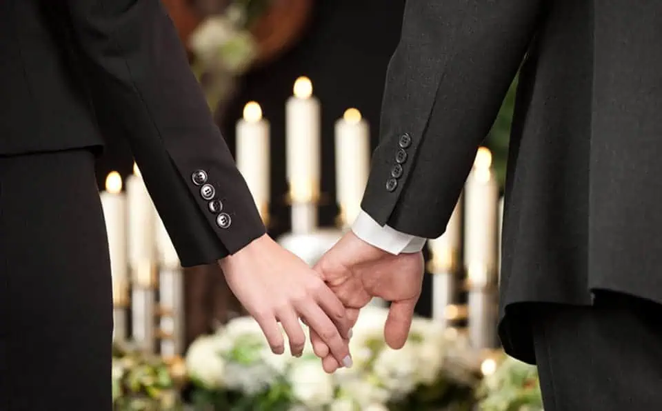 Two people holding hands at a memorial service with candles in the background.