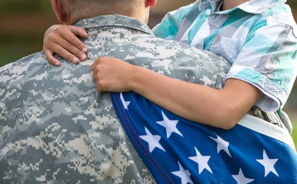 A soldier in camouflage uniform with a child holding an American flag.