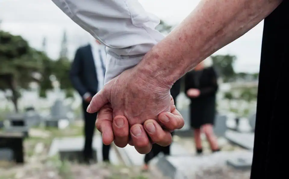 Close-up of two people holding hands at a memorial site.
