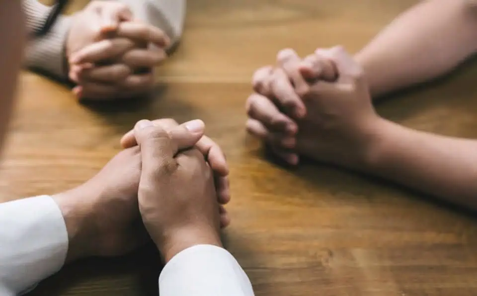 People holding hands in prayer at a memorial gathering.