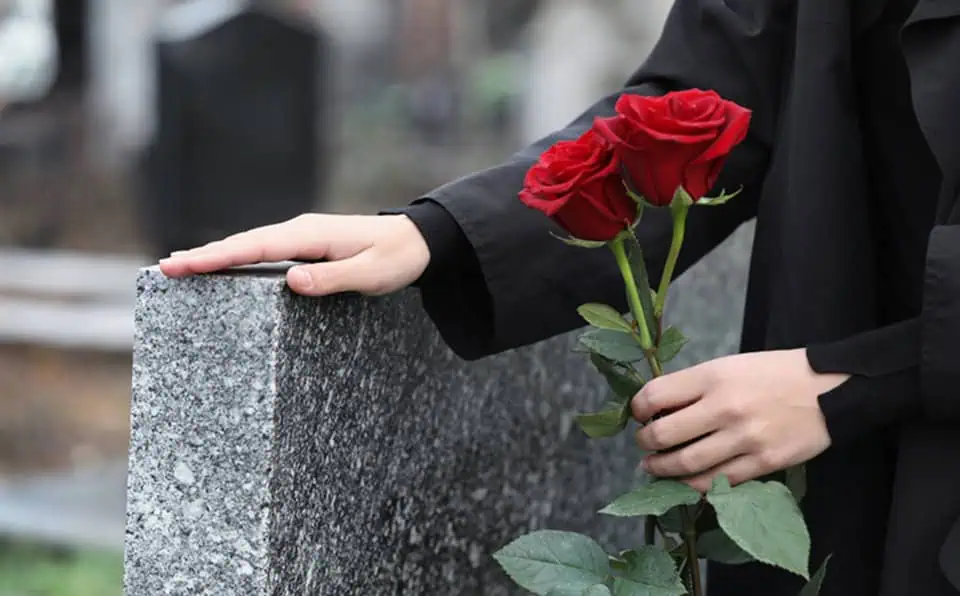 Person placing red roses on a grave at Mountain View Memorial Park.