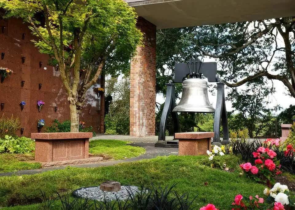 Large bell sculpture with garden benches and colorful flowers.