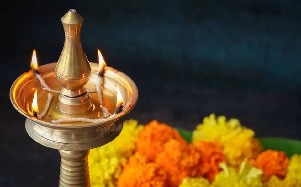 Oil lamp with lit flames and marigold flowers in the foreground.