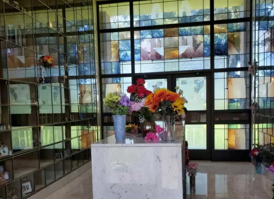 Indoor memorial display with colorful flowers and glass wall backdrop.