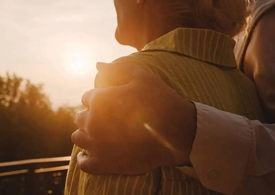 Close-up of two people embracing outdoors during sunset at memorial grounds.
