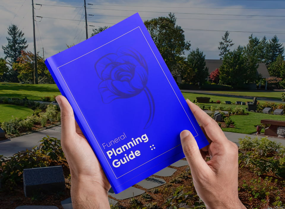 Person holding a blue funeral planning guide in a cemetery setting.