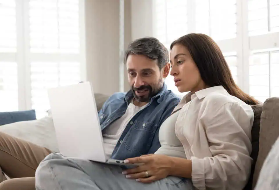 Man and woman watching a laptop together in a bright room.