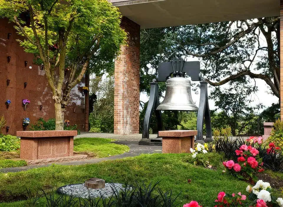 Outdoor memorial garden with a large bell, benches, and colorful flowers.