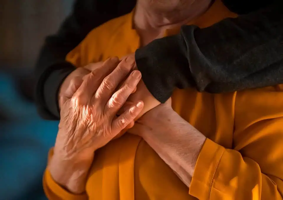 Close-up of two hands holding each other, one elderly and one younger, in a comforting gesture.