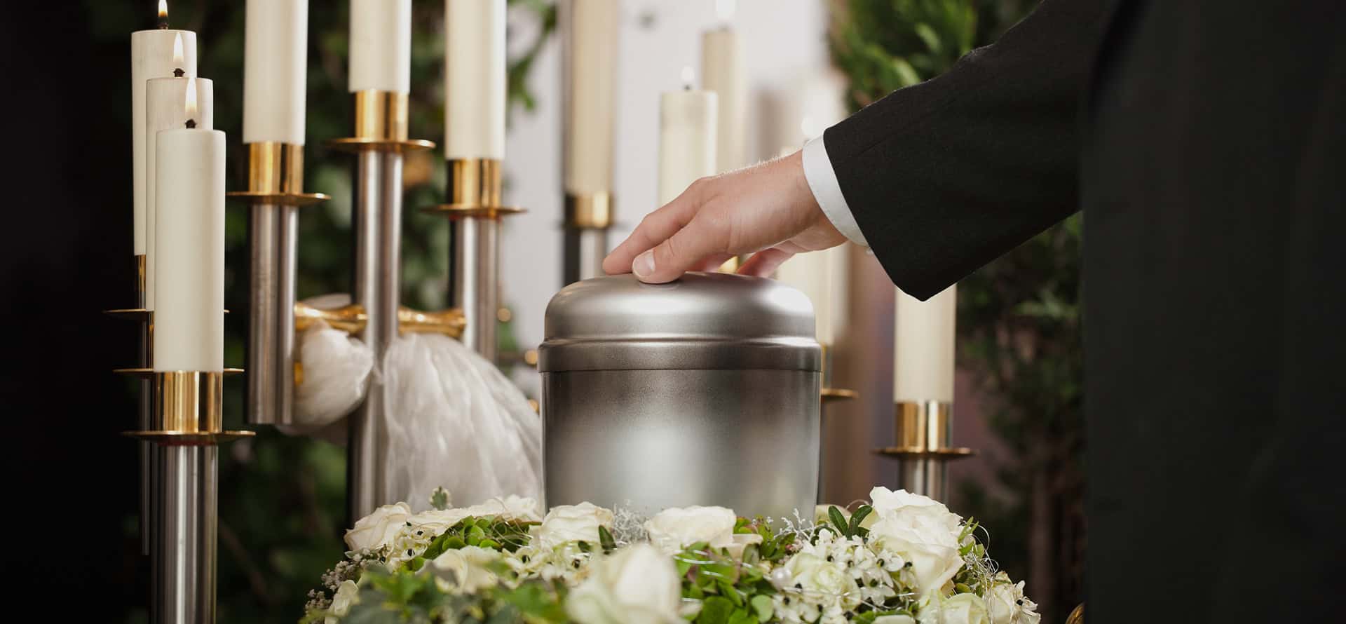 Person in formal attire places a casket on a table with candles and flowers.