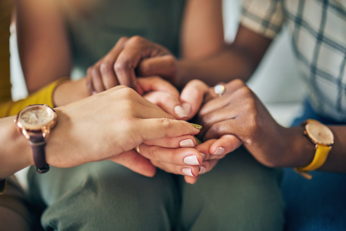 Close-up of hands of three people holding each other.